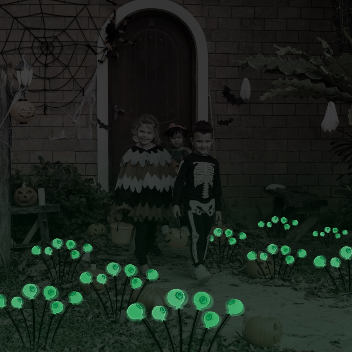 Trick or treaters walking past green solar eyeball path lights at a decorated front door